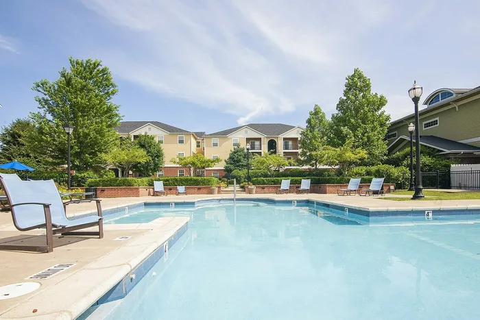 Inviting apartment community with a sparkling outdoor pool, surrounded by plush greenery and contemporary seating, perfect for relaxation.
