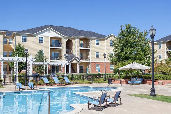 Inviting apartment complex with a sparkling pool, cozy loungers, and vibrant landscaping under a clear blue sky.