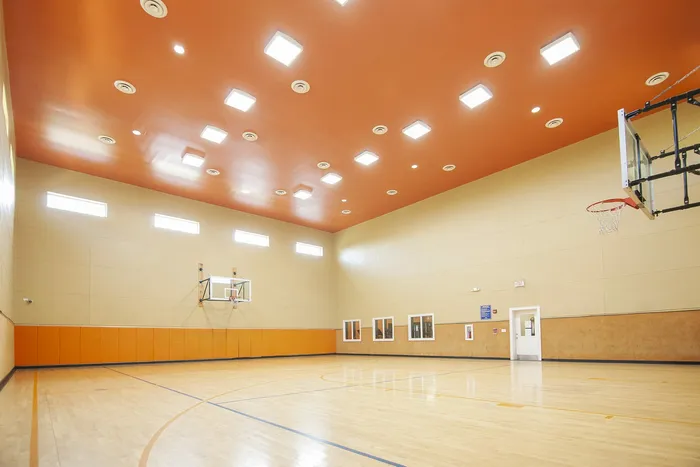 Spacious indoor basketball court with polished hardwood floors and vibrant orange accents, ideal for sports enthusiasts.