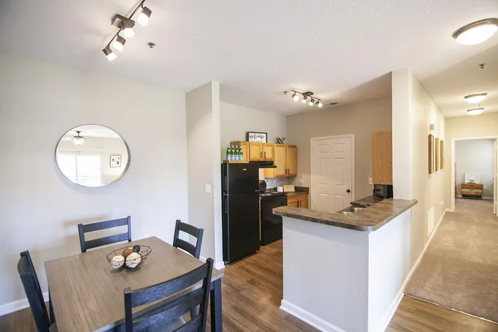 Charming open-plan apartment featuring a cozy dining area, modern kitchen with sleek black appliances, and warm wooden cabinets.