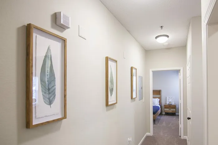 Inviting hallway adorned with stylish framed leaf art leading to a cozy bedroom, offering modern comfort and elegance.