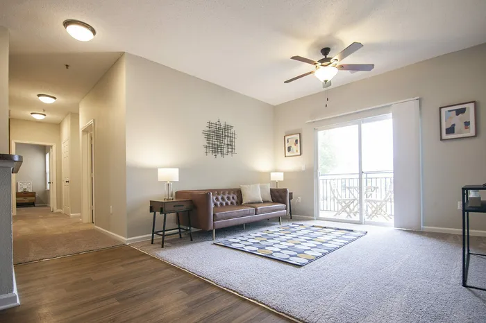 Modern, sunlit living room with a stylish ceiling fan, cozy brown leather sofa, and elegant decor, leading to a charming balcony view.