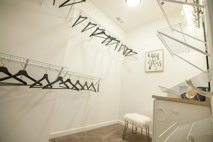 Spacious walk-in closet with sleek shelving and ample hangers, featuring a cozy stool and modern artwork, offering luxurious storage solutions.