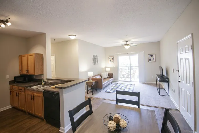 Bright open-concept living area with stylish kitchen, inviting lounge, and natural light pouring through glass doors leading to a cozy balcony.