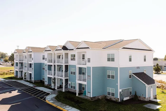 Charming three-story apartment building with blue and white exterior, featuring private balconies and lush landscaping in a serene neighborhood.