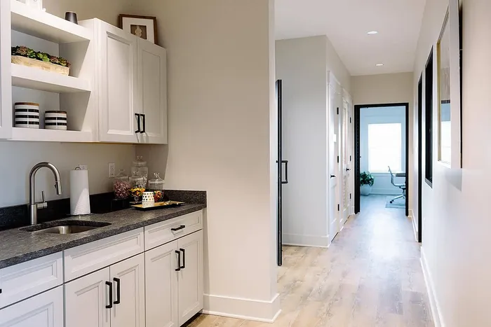 Chic and modern hallway with white cabinetry, sleek countertops, and a bright workspace in the distance.