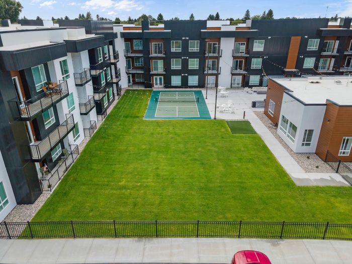 Modern apartment complex with stylish balconies overlooking a lush green courtyard and tennis court, perfect for relaxed living.