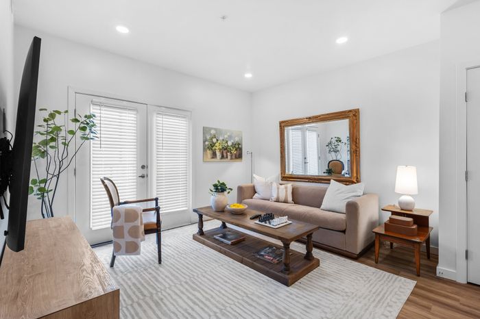 Charming living room with a cozy beige sofa, elegant wooden coffee table, and vibrant potted plants, flooded with natural light from French doors.