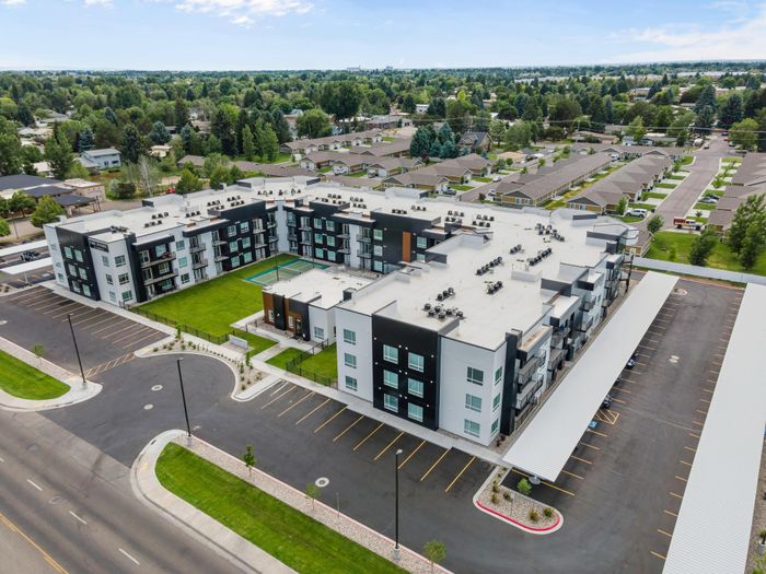Bird's eye view of a modern apartment complex with a green courtyard and ample parking, set in a lush suburban neighborhood.