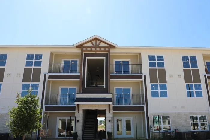 Contemporary three-story apartment building with stylish balconies and large windows set against a clear blue sky.