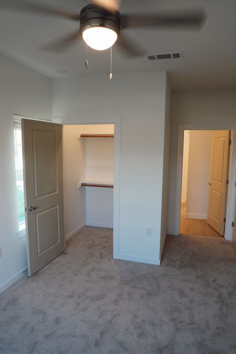 Bright bedroom with cozy carpet flooring, featuring a spacious closet and elegant ceiling fan.