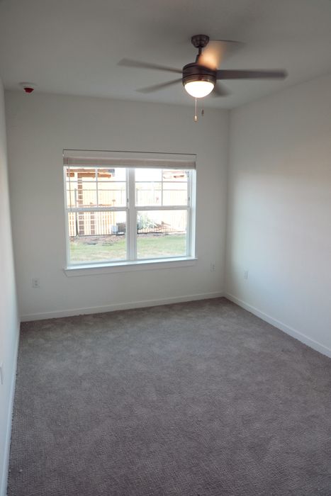 Bright, cozy room with soft carpet, large window for natural light, and modern ceiling fan, ideal for relaxation.