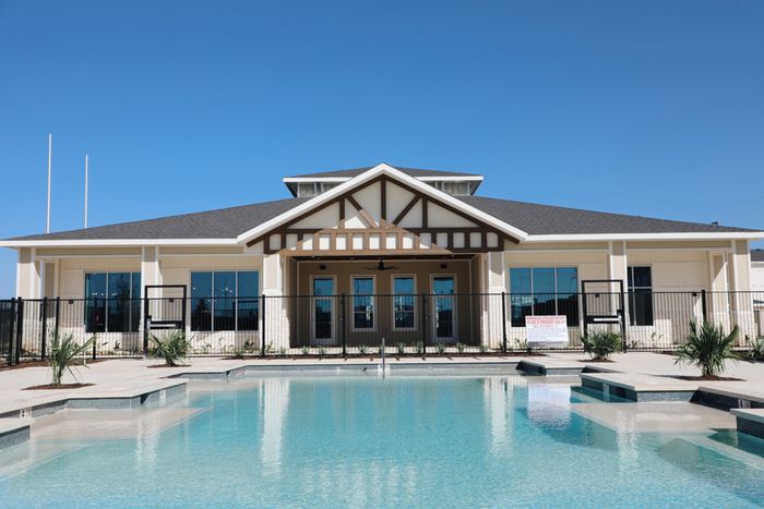 Elegant community clubhouse with a shimmering pool and modern architectural design under a clear blue sky.