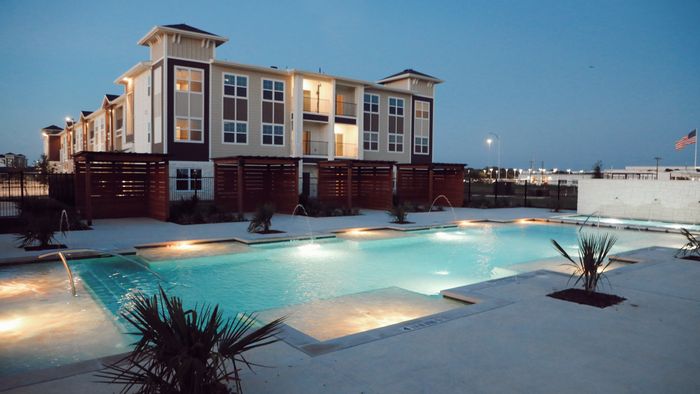 Pool courtyard at blue hour with private cedar cabanas and a three-story residential building behind