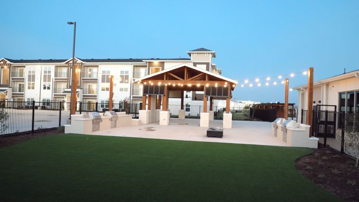 Covered outdoor pavilion with string lights, gas grills, and an artificial turf lawn at dusk