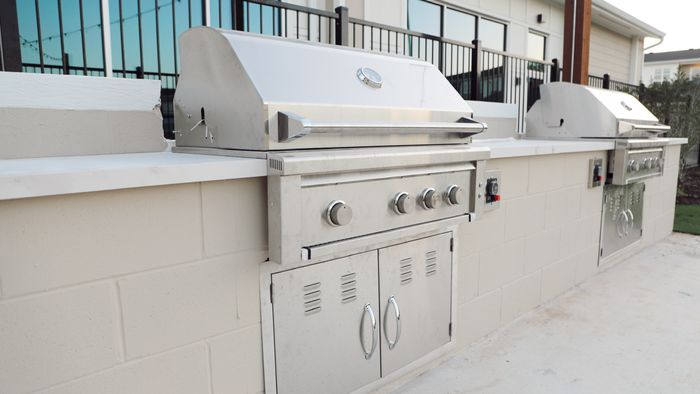 Two built-in stainless steel grills set into a stone outdoor kitchen counter