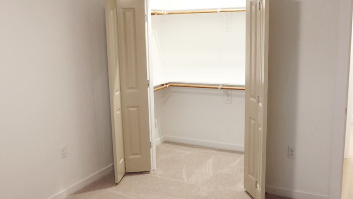 Carpeted bedroom with open double doors revealing a shelved closet