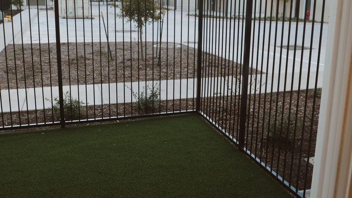 Private fenced yard with artificial turf viewed from a ground-floor apartment doorway