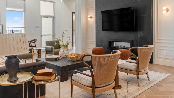 Upscale clubhouse lounge featuring a modern fireplace set in a black tile wall beneath a large TV, surrounded by stylish armchairs, a dark sofa, and a heavy wooden coffee table.