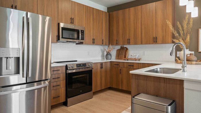 Interior view of a contemporary apartment kitchen showcasing flat-panel wood-look cabinetry, a white subway tile backsplash, white countertops, and premium stainless steel appliances.