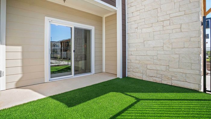 Private ground-floor apartment patio featuring an artificial turf yard space, an Austin stone exterior wall, and sliding glass doors.