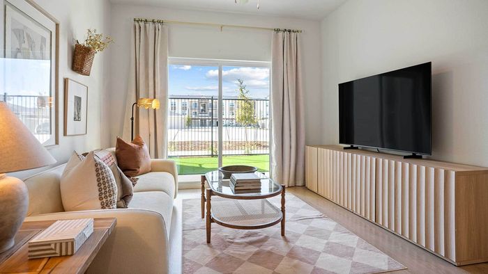 Bright apartment living room featuring a white sofa, a large flat-screen TV on a modern wooden console, and sliding glass doors leading to a private fenced patio.