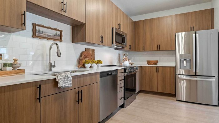 Full view of a luxury apartment kitchen showcasing extensive wood-grain cabinetry, a white tile backsplash, white quartz countertops, and a full suite of stainless steel appliances.
