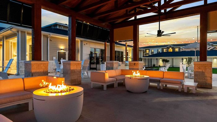 Covered outdoor lounge at Entrada at San Marcos featuring stone fire pit, plush seating, and warm twilight lighting.