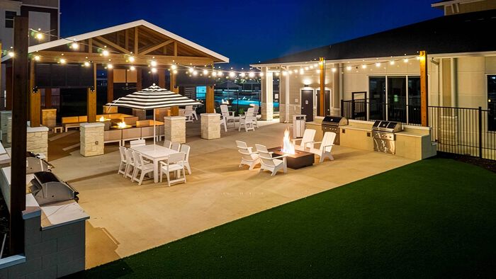 Elevated twilight view of outdoor grilling stations, fire pits, dining tables, and turf lawn at Entrada luxury apartments.