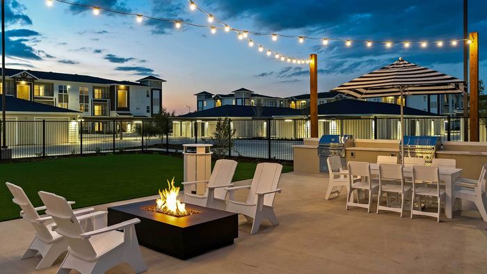 Twilight outdoor dining area with string lights, Adirondack chairs around a fire pit, and stainless steel grills at Entrada at San Marcos.