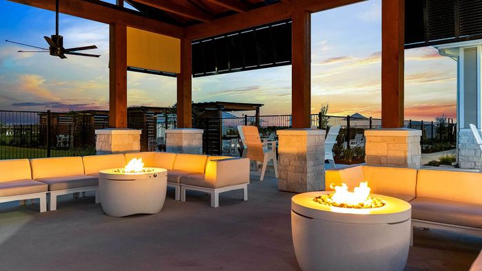 Modern outdoor fire pit tables and seating area beneath a wooden pavilion at Entrada luxury apartments in San Marcos.