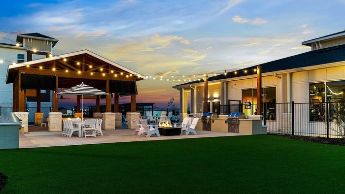 Wide twilight view of Entrada at San Marcos outdoor amenity courtyard with turf lawn, string lights, and outdoor grilling stations.