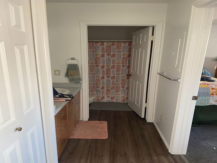 Inviting bathroom view with elegant wood flooring, a stylish shower curtain, and a cozy bedroom glimpse.