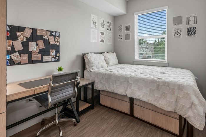 Cozy bedroom with a stylish desk, organized bulletin board, and bright window views.