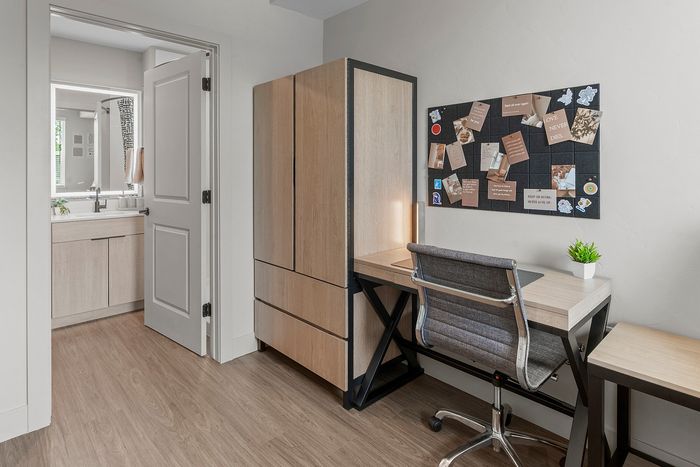 Contemporary home office featuring a sleek desk, modern chair, and organized pinboard, adjacent to a stylish bathroom with natural wood finishes.