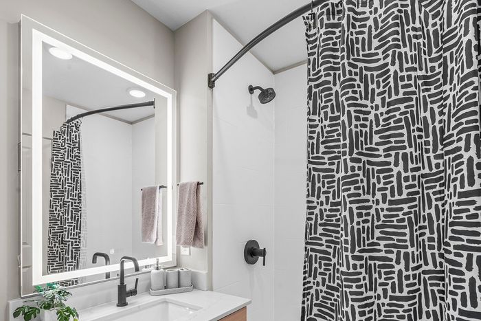 Modern bathroom featuring elegant black and white patterned shower curtain, illuminated mirror, and sleek fixtures for a luxurious touch.