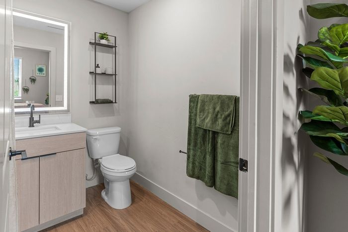 Modern bathroom with sleek vanity, elegant mirror lighting, and lush green towel accents.