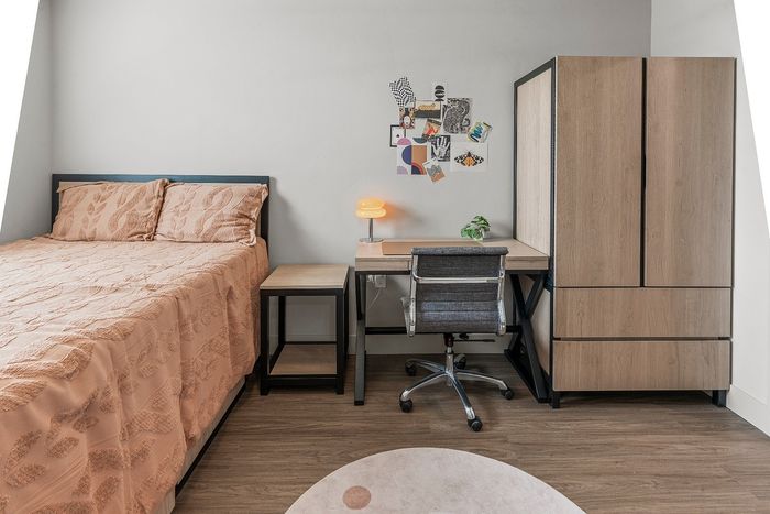 Modern bedroom featuring a cozy bed with artistic decor, sleek wooden workspace, and stylish wardrobe, all on elegant wooden flooring.