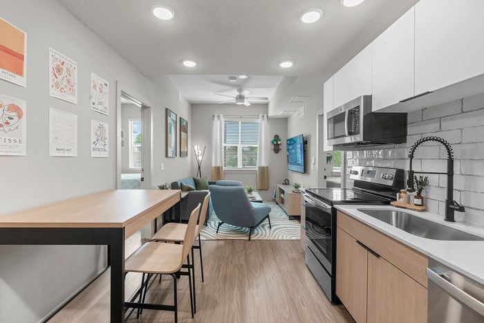 Modern apartment interior featuring a stylish open-concept kitchen and living room, with sleek appliances, cozy seating, and contemporary artwork.