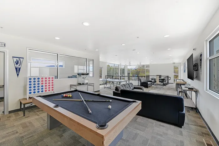Spacious and inviting recreation room featuring a pool table, cozy couches, large windows with scenic views, and ample seating for entertainment.