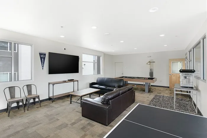 Modern living space with sleek black sofas, large flat-screen TV, pool table, and stylish ping pong area, perfect for relaxation and entertainment.
