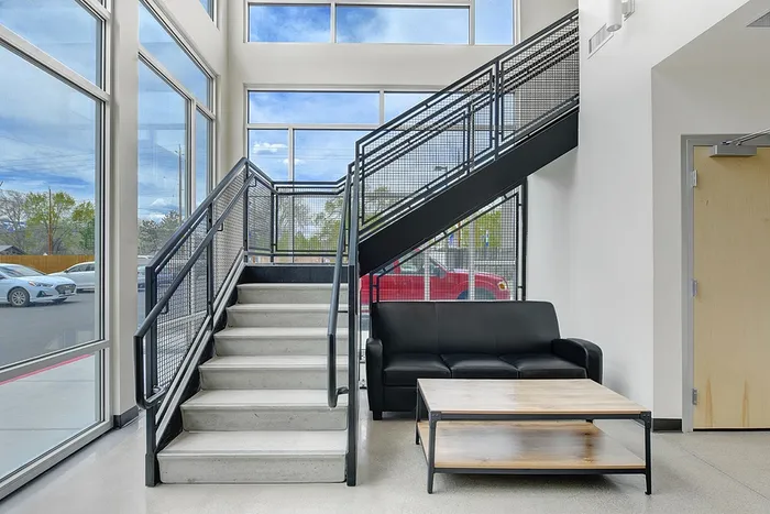 Modern lobby with sleek staircase, large windows, and cozy black sofa under bright natural light.