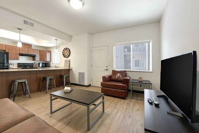 Modern open-concept living area with sleek kitchen, cozy leather armchair, and large flatscreen TV.