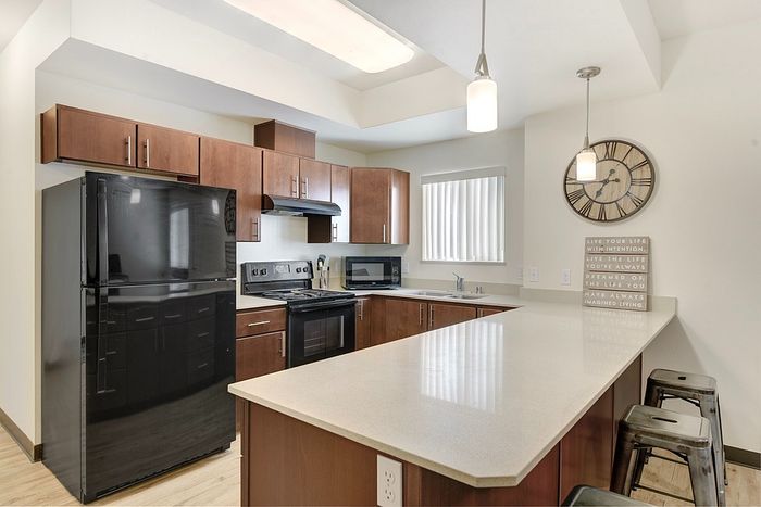 Modern kitchen with elegant wooden cabinets, sleek black appliances, and a spacious island counter featuring stylish pendant lighting and chic bar stools.