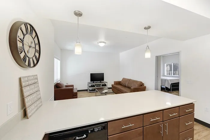 Modern open-concept living area with a sleek kitchen counter, cozy leather sofas, and a wall-mounted clock, offering inviting comfort.