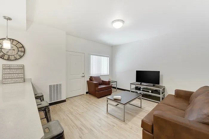 Inviting living room with modern decor, featuring comfortable brown leather seating, sleek coffee table, and flat-screen TV, offering a warm and cozy ambiance.