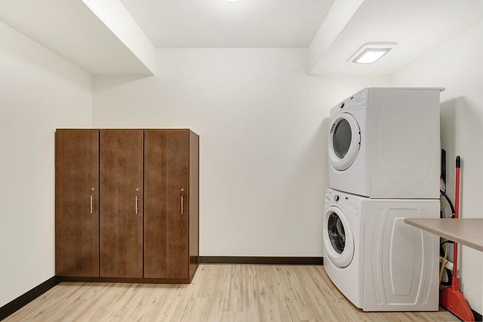 Modern laundry room featuring a stacked washer and dryer set alongside sleek wooden cabinetry, with polished wood flooring enhancing the inviting space.