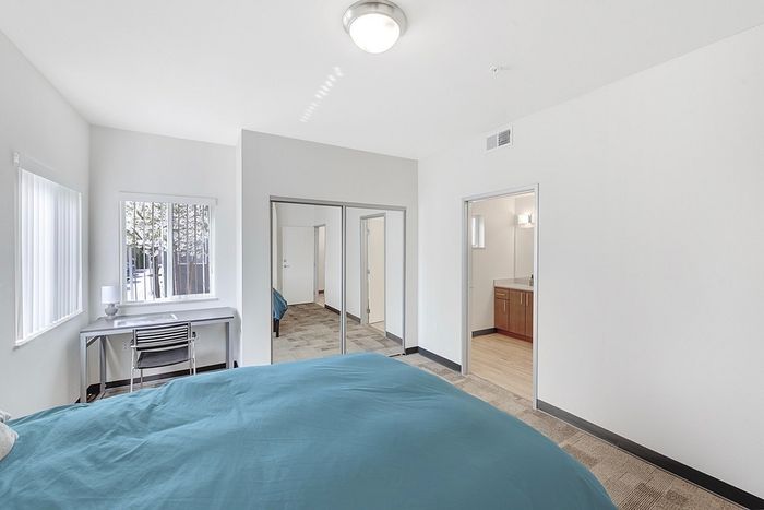 Bright and spacious bedroom with large windows, featuring a comfortable bed, mirrored closet doors, and a connected modern bathroom.