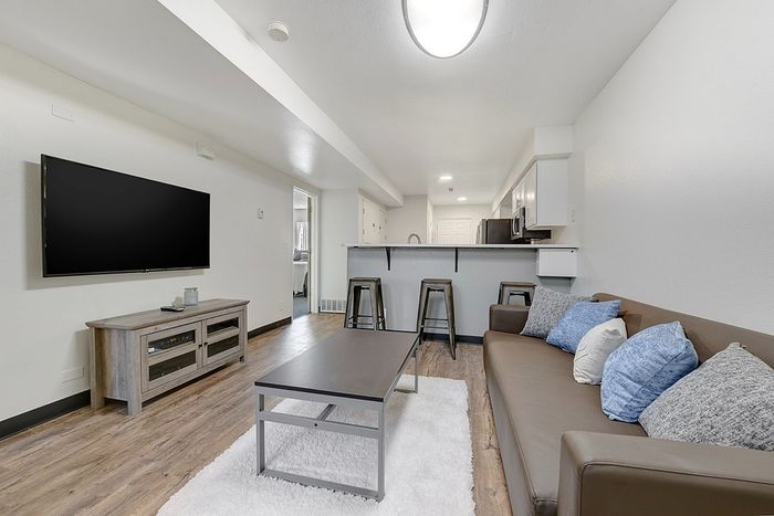 Modern living area with a sleek leather sofa, stylish coffee table, and open-plan kitchen featuring a breakfast bar with stools, creating a cozy yet contemporary atmosphere.