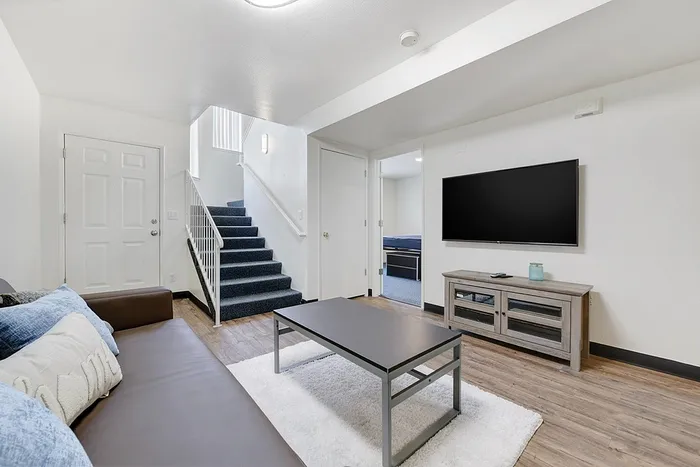 Modern living room with sleek wooden floors and stylish furnishings, complete with a cozy staircase leading to upper levels and a wall-mounted TV for entertainment.